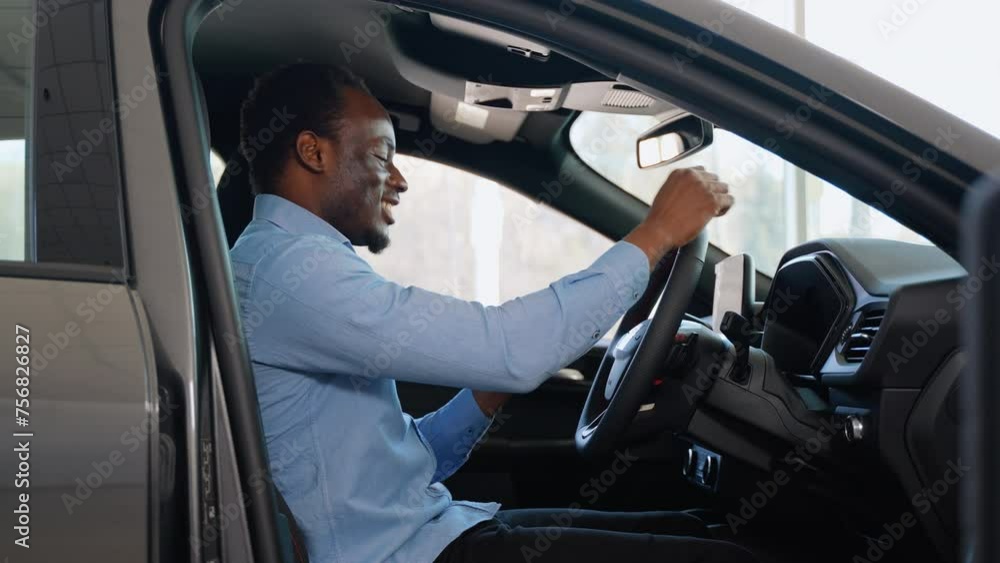 African american man shows emotions of happiness while sitting in his new electric car. The buyer selects a car. Right hand drive car African american man shows emotions of happiness while sitting in his new electric car. The buyer selects a car. Right hand drive car