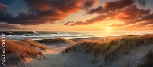 The sky is painted with vibrant hues as the sun sets over the beach, casting a warm glow on the sand dunes in the foreground