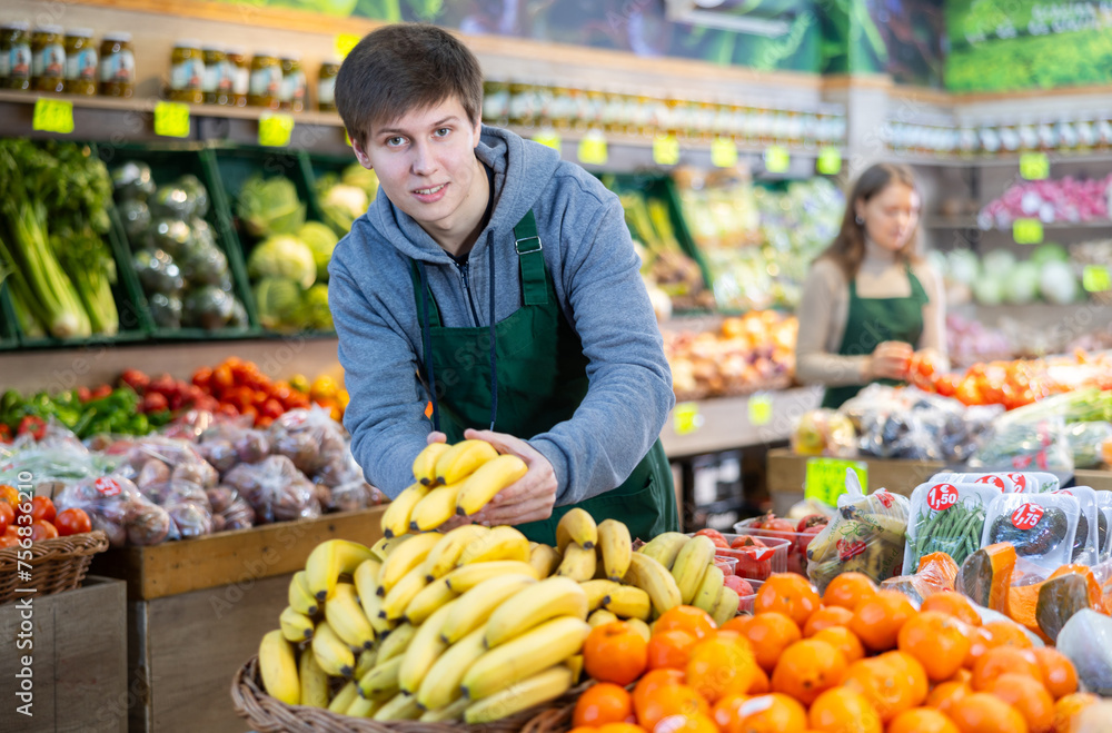 Positive male seller in apron displaying assortment of bananas at supermarket