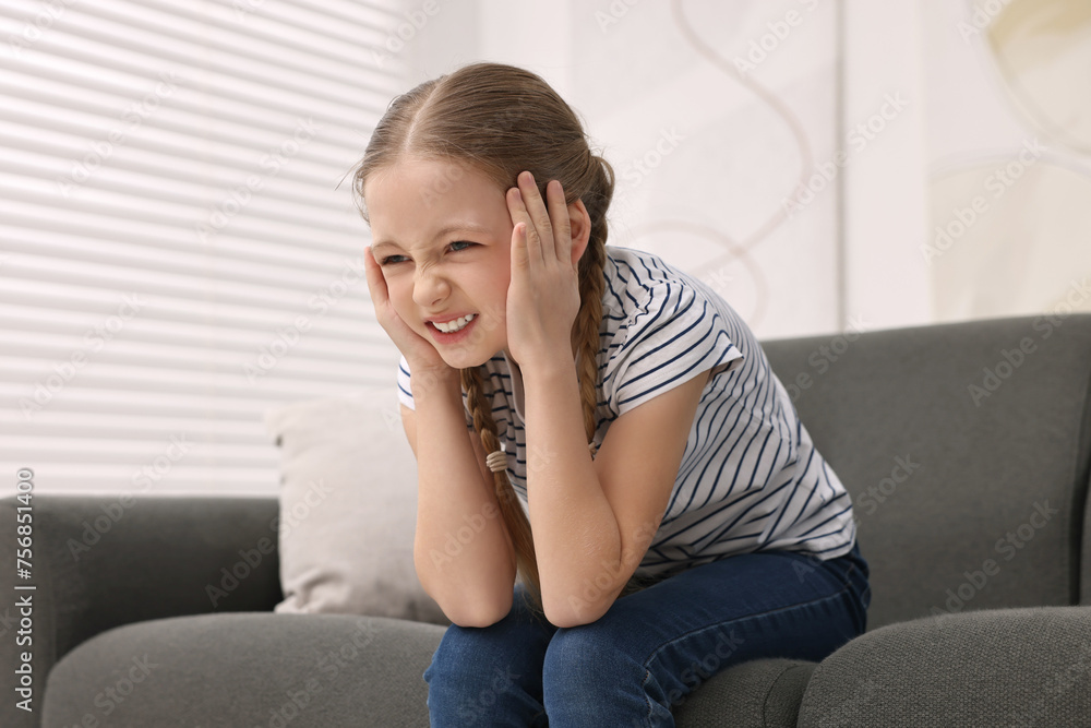 Little girl suffering from headache on sofa indoors Little girl suffering from headache on sofa indoors
