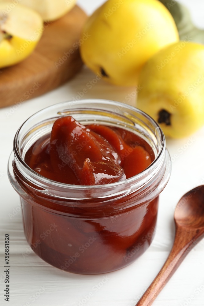 Tasty homemade quince jam in jar, spoon and fruits on white wooden table, closeup Tasty homemade quince jam in jar, spoon and fruits on white wooden table, closeup