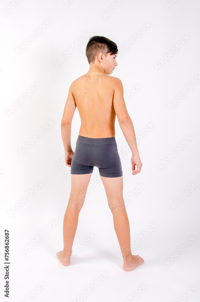 Fototapeta premium Preteen male fitness model standing shirtless with arms at his side, back turned to camera
