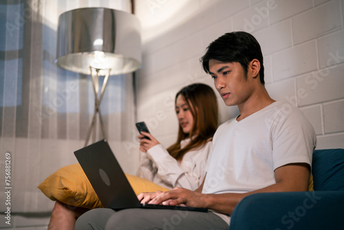 Asian young man work at home with his wife using mobile phone at night. 