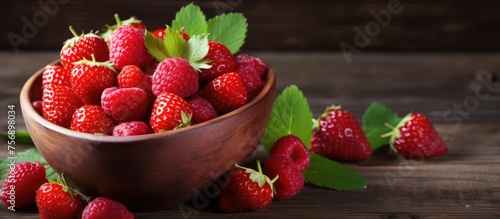 Fresh raspberries and strawberries displayed in a rustic wooden bowl on a wooden table. These natural foods can be used as ingredients in various recipes to create delicious dishes