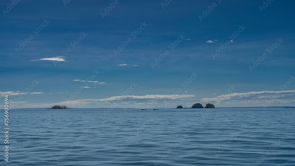 A serene seascape. Ripples on the surface of a calm blue ocean. Islands are visible on the horizon. Clouds in the azure sky. Madagascar.