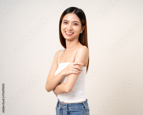 Vaccination. Young beautiful asian woman getting a vaccine protection the coronavirus. Smiling happy female showing arm with bandage after receiving vaccination. On isolated white background. © Chanakon