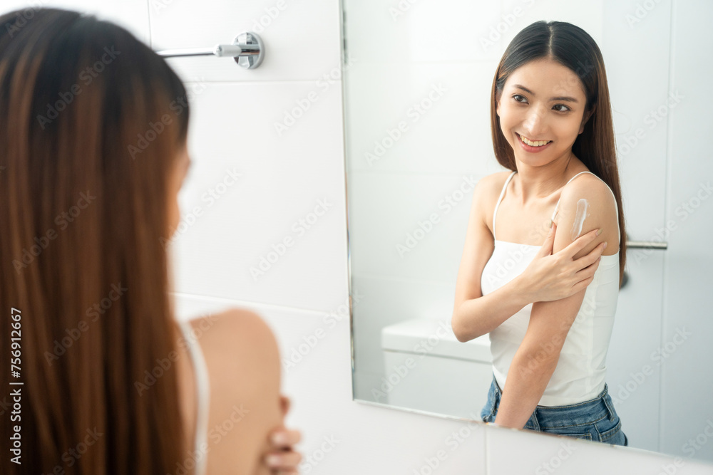 Beautiful smiling happy young asian woman with beauty skin care treatment lotion on the body. Charming female lady looking mirror applying body cream Facial treatment beauty and spa Beautiful smiling happy young asian woman with beauty skin care treatment lotion on the body. Charming female lady looking mirror applying body cream Facial treatment beauty and spa