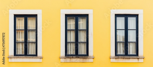 Three rectangular windows with amber tints are fixtures on the symmetrical facade of a yellow building with white trim. The composite material used for the windows adds to the overall aesthetic