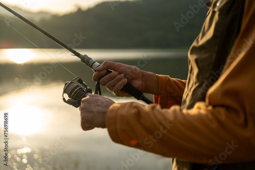 Enjoy moment of Handsome man fishing as a leisure activity during his vacation at the lake on sunset. Silhouette at sunset moment of man fishing rotation with reel.