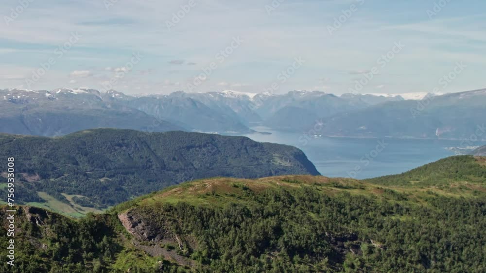 Aerial shot, soaring over a tree lined ridge, in Norway, revealing snow capped mountains and a Fjord in the background. Aerial shot, soaring over a tree lined ridge, in Norway, revealing snow capped mountains and a Fjord in the background.
