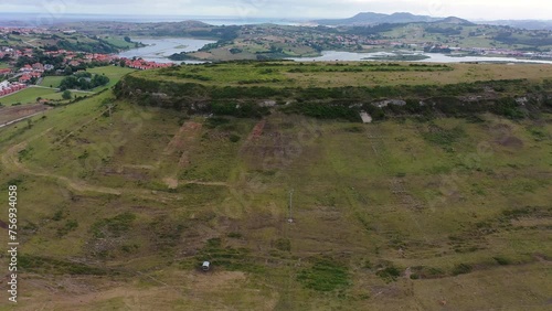 Lateral flight showing the remains of a Paleolithic settlement in a green area and surrounded by an urban area and mountains with the mouth of the river to the sea in Cantabria Spain