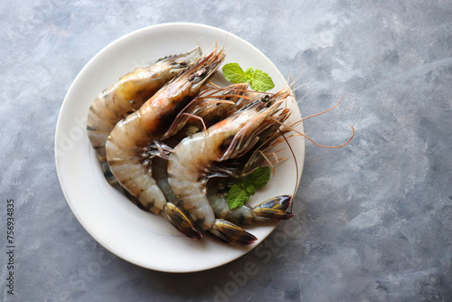 Fresh shrimp or black tiger prawns. Uncooked on a white ceramic plate with coriander and mint leaves. on a moody background with copy space. Kolambi in Marathi. photo