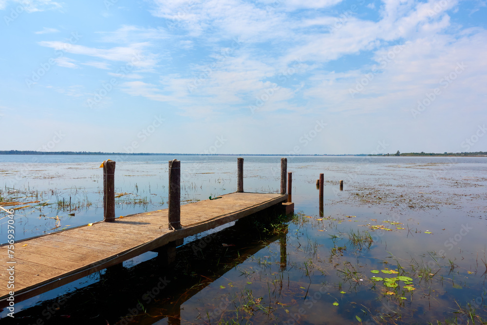 A wooden pier on a large pond with small cornices surrounding it.