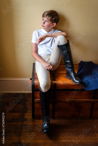 A young equestrian rider in boots and riding pants sitting and thinking about his next competition

 photo