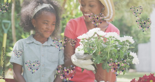 Image of hearts over smiling african american mother and daughter gardening plants