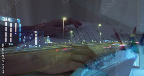 Image of hands working on laptop over sped up traffic in city at night