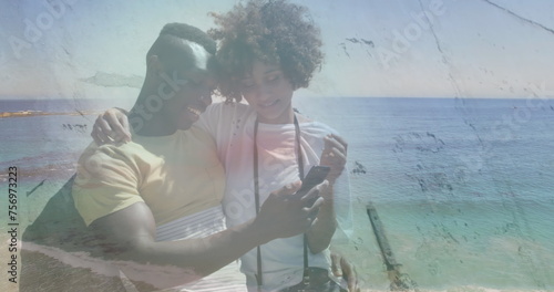 Image of happy african american couple using smartphone at beach over sea