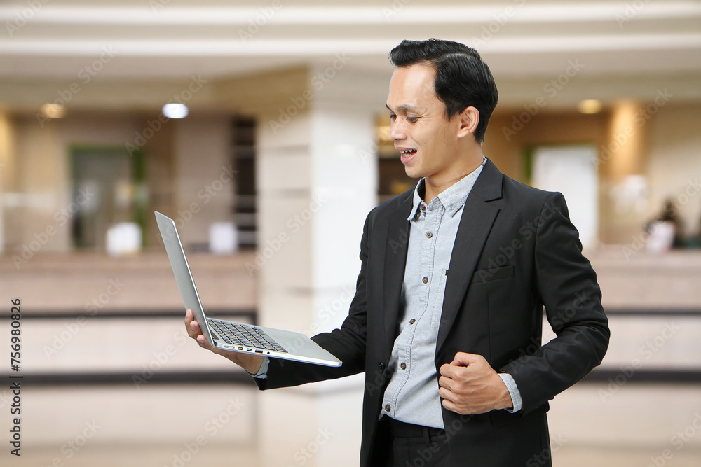 Happy asian indonesian business man in suit holding laptop computer in the lobby Happy asian indonesian business man in suit holding laptop computer in the lobby