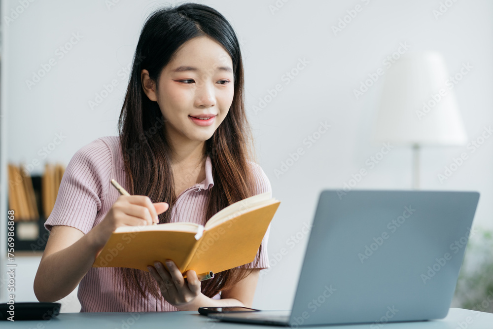Female use a Laptopand take notes in the notebook at the office desk in the morning. Female use a Laptopand take notes in the notebook at the office desk in the morning.