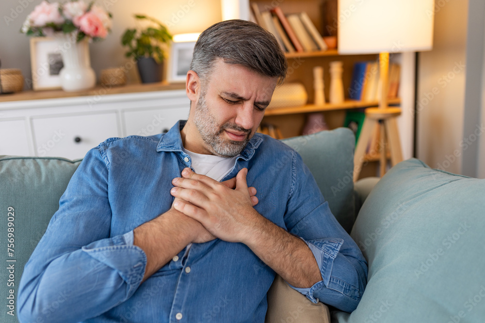 Man presses hand to chest has heart attack suffers from unbearable pain, Mature man with pain on heart in living room. man suffering from bad pain in his chest heart attack at home