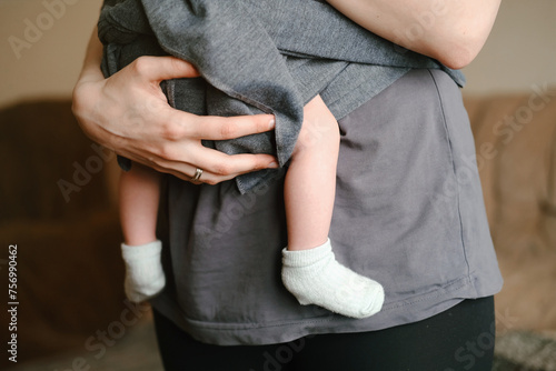 Mother with ergo baby carrying toddler at home in sling. While baby is sleeping. Tiny little feet in socks.  © leriostereo