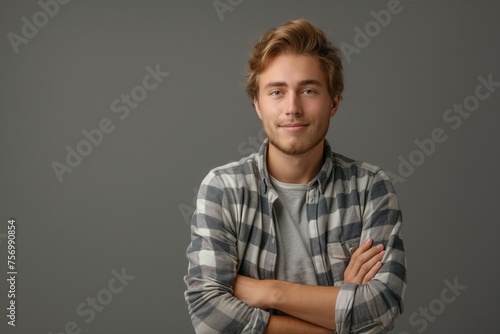 Young confident man with a charming smile wearing a plaid shirt and posing with arms crossed, concept of youth confidence and casual style