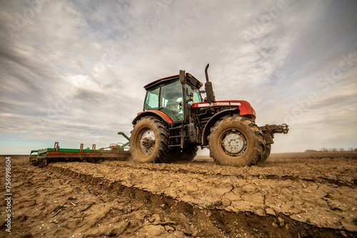 Agricultural scene of a tractor plowing dry soil, kicking up dust with a dramatic sky overhead