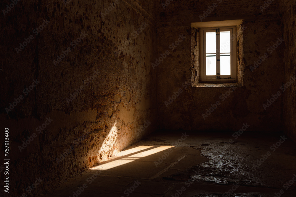 Old empty room with stone walls, almost in darkness, with the only light from the window that can be seen as it is projected on the floor and the wall. - obrazy, fototapety, plakaty 