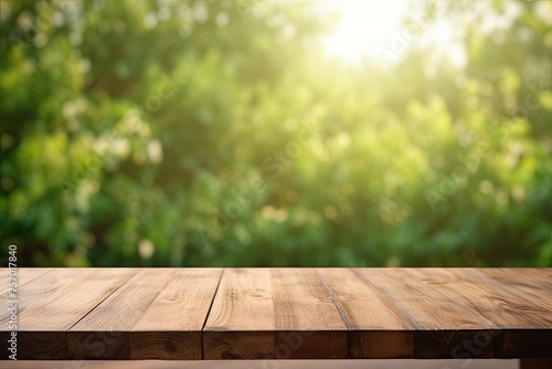 An unoccupied wooden table surface is seen against a blurry, abstract green backdrop from the garden and house in the early morning.