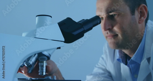 Caucasian scientist examines samples under a microscope in a lab