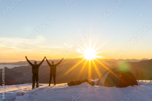 Couple celebrating next to tent in snow at sunset. High quality photo
