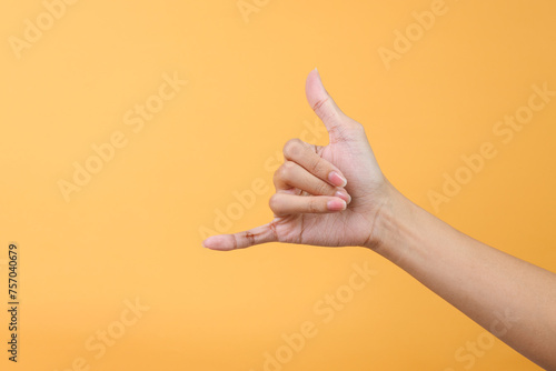 Woman hand showing calling hand gesture or shaka sign on yellow background photo
