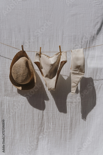 Female swimwear and straw hat hanging over white cotton cloth with strong shadows. Sunbathing on a summer sunny day concept