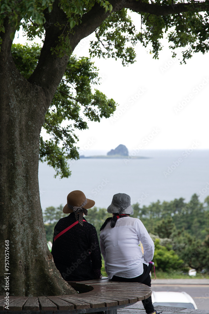 View of mother and daughter sitting on the bench by the tree