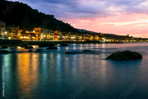 evening or night landscape of evening town coastline in golden lights and sea gulf with calm water and nice reflections with beautisul sunset sky on background photo