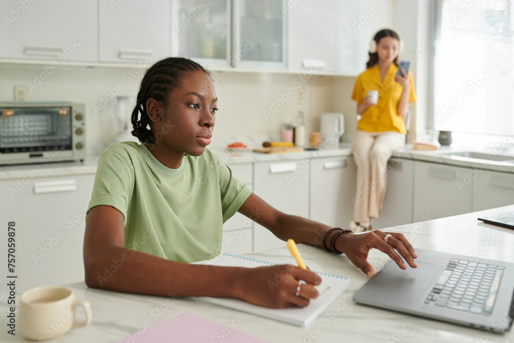 Black college student working on laptop at kitchen counter Black college student working on laptop at kitchen counter