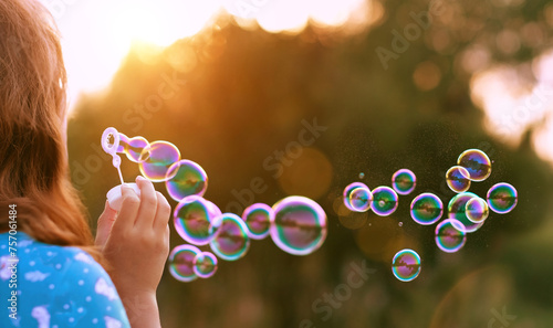 girl blowing soap bubbles outdoor, blurred natural sunny background. rear view. dreaming, harmony peaceful atmosphere. Happy childhood concept.