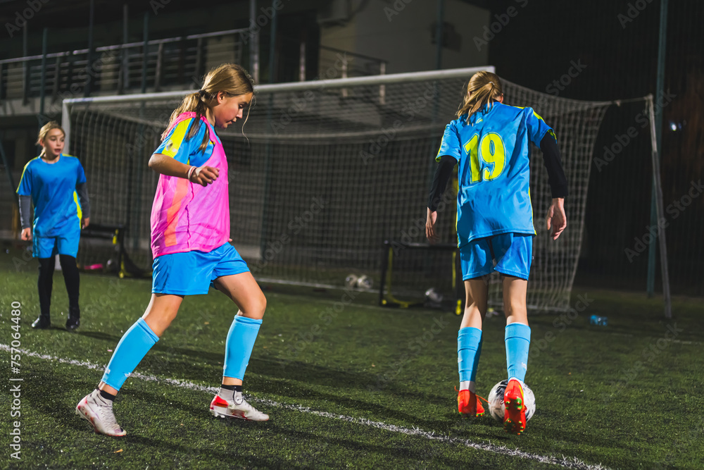 Fototapeta premium young girls in blue uniforms practicing football in the late evening, team sport concept. High quality photo