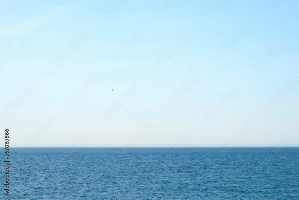 Airplane plane flying over the sea in clear blue sky at sunny weather. Passenger jet approaching to land at airport. Tourism, travel, journey, wanderlust concept, air flight. Calm blue sea on summer.