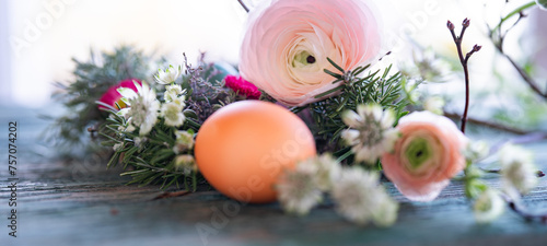 Easter egg in front of a herb nest with spring flowers on weathered rustic wooden table. Close-up with short depth of field. Horizontal easter background.