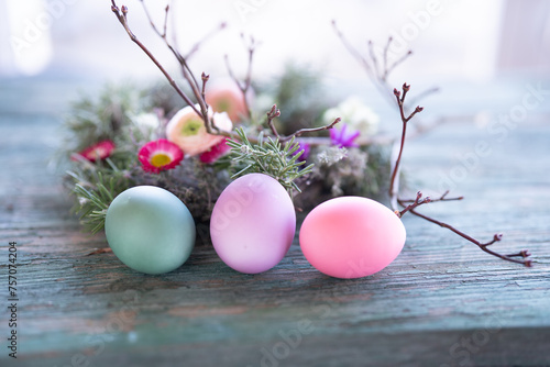 Colorful easter eggs in front of a herb nest with spring flowers on weathered rustic wooden table. Close-up with short depth of field. Easter background.
