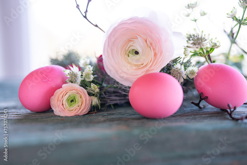 Pink easter eggs in front of a herb nest with spring flowers on weathered rustic wooden table. Close-up with short depth of field. Easter background.
