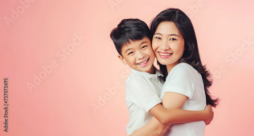 Young asian mother and son hugging and smiling in front of a pink background with copy space for Happy Mothers Day banner or flyer design