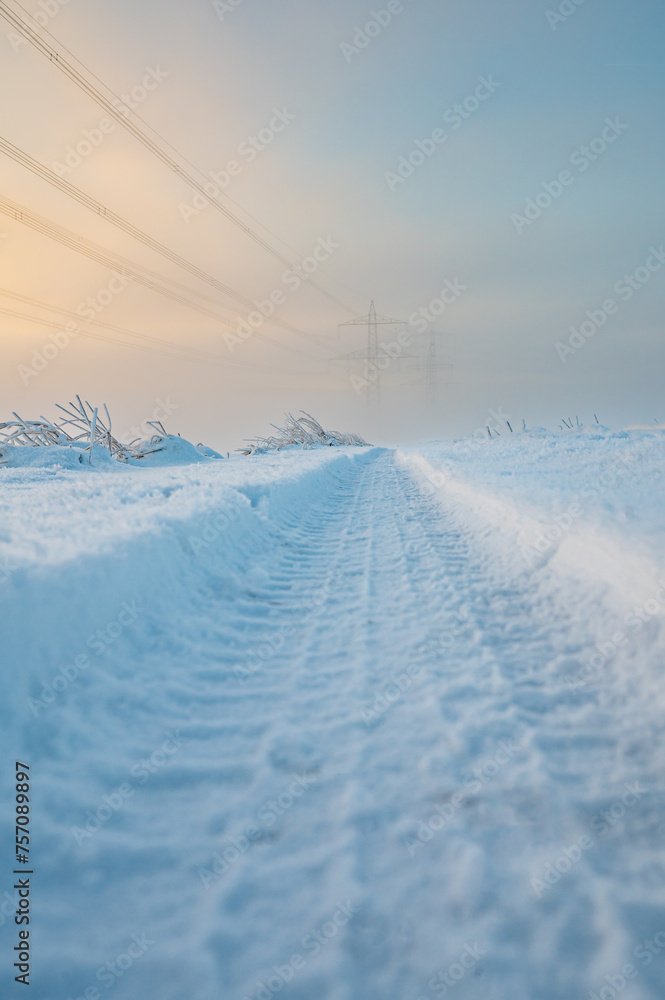 Fahrspur zu Strommasten im Schnee bei Sonnenaufgang, Hünfelden. Hessen, Deutschland
