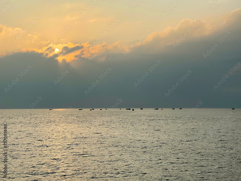 Beautiful sunset on the sea, the sun sets behind a large cloud lying on the water