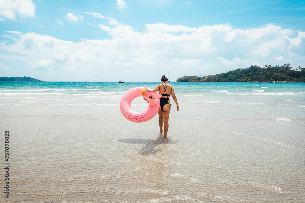 Summer travel, woman holding an inner tube, walking in the middle of the sea
