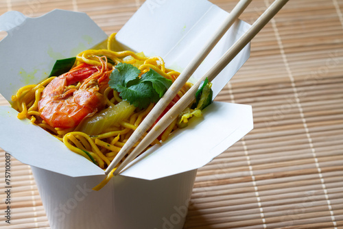 Chinese noodles with shrimps and vegetables in box on bamboo mat. Chinese food concept
