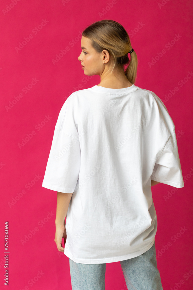 Beautiful blonde girl in a white oversized T-shirt and blue jeans posing on a gray background