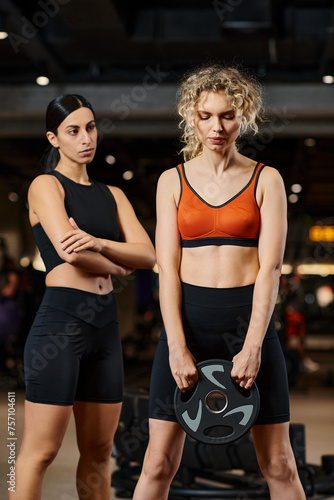 appealing athletic female coach in black sportwear explaining how to use weight plate to her client © LIGHTFIELD STUDIOS