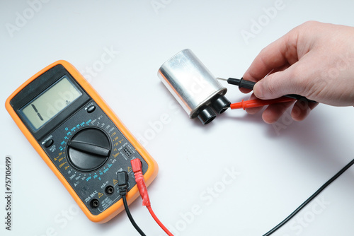 Diagnostics repair of microwave oven. The hands of the master checking the high-voltage power capacitor and magnetron with multimeter photo